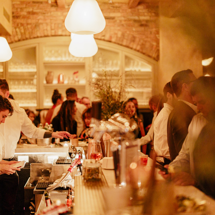 A lively restaurant scene with a bar, patrons, and staff in a warm, inviting atmosphere.