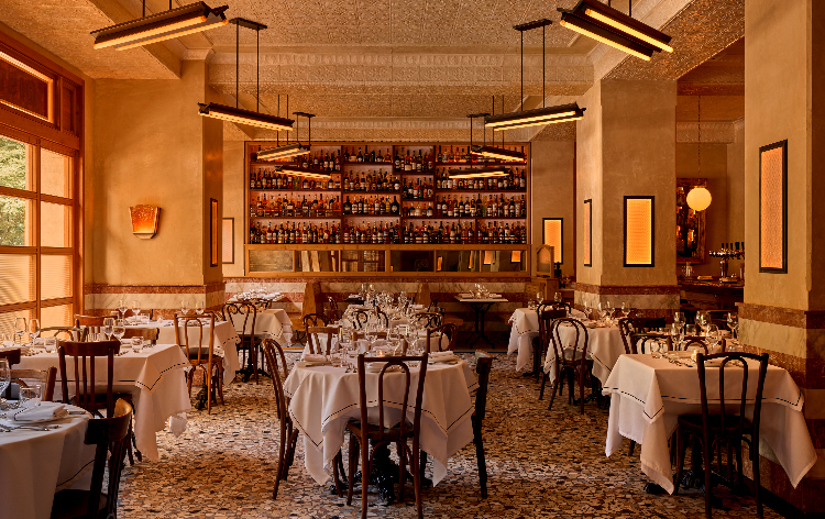 Elegant restaurant interior with multiple wine racks, tables set for dining, and ornate ceiling lights.